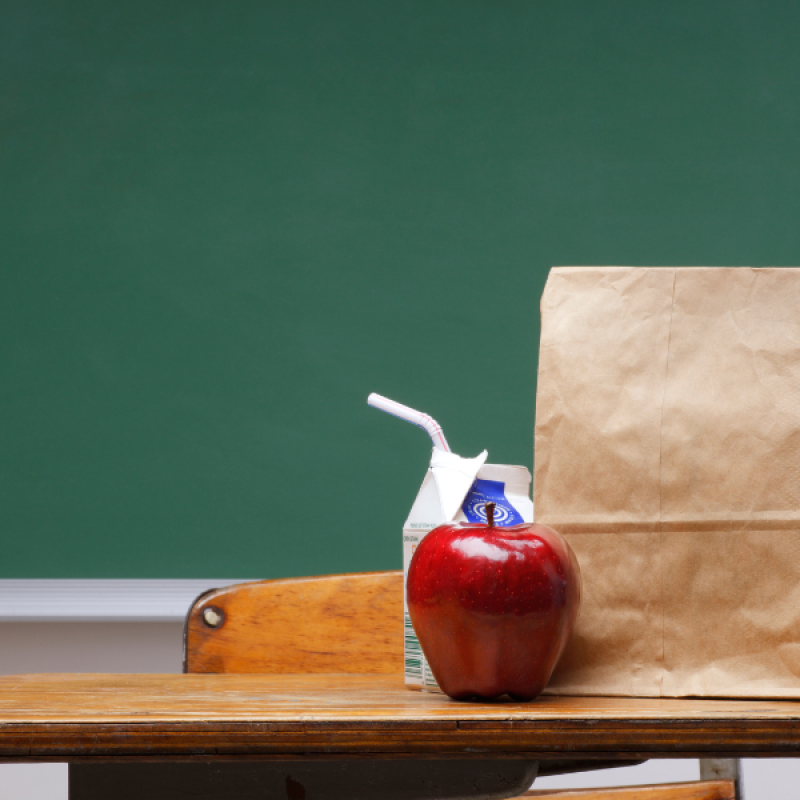 apple, milk carton, brown paper bag on desk, chalkboard background